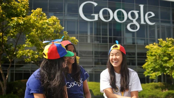 Googlers sitting infront of google HQ with a Noogler hat hats